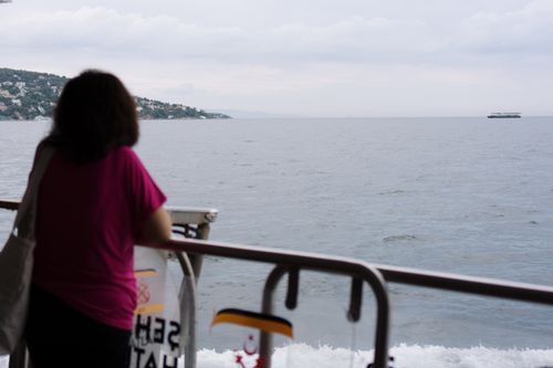 Free A person in a pink shirt looks out over a calm sea from a ferry, with distant hills visible. Stock Photo