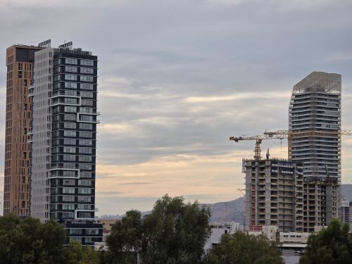 Free Modern high-rise buildings with construction cranes against a cloudy sky, representing urban development. Stock Photo