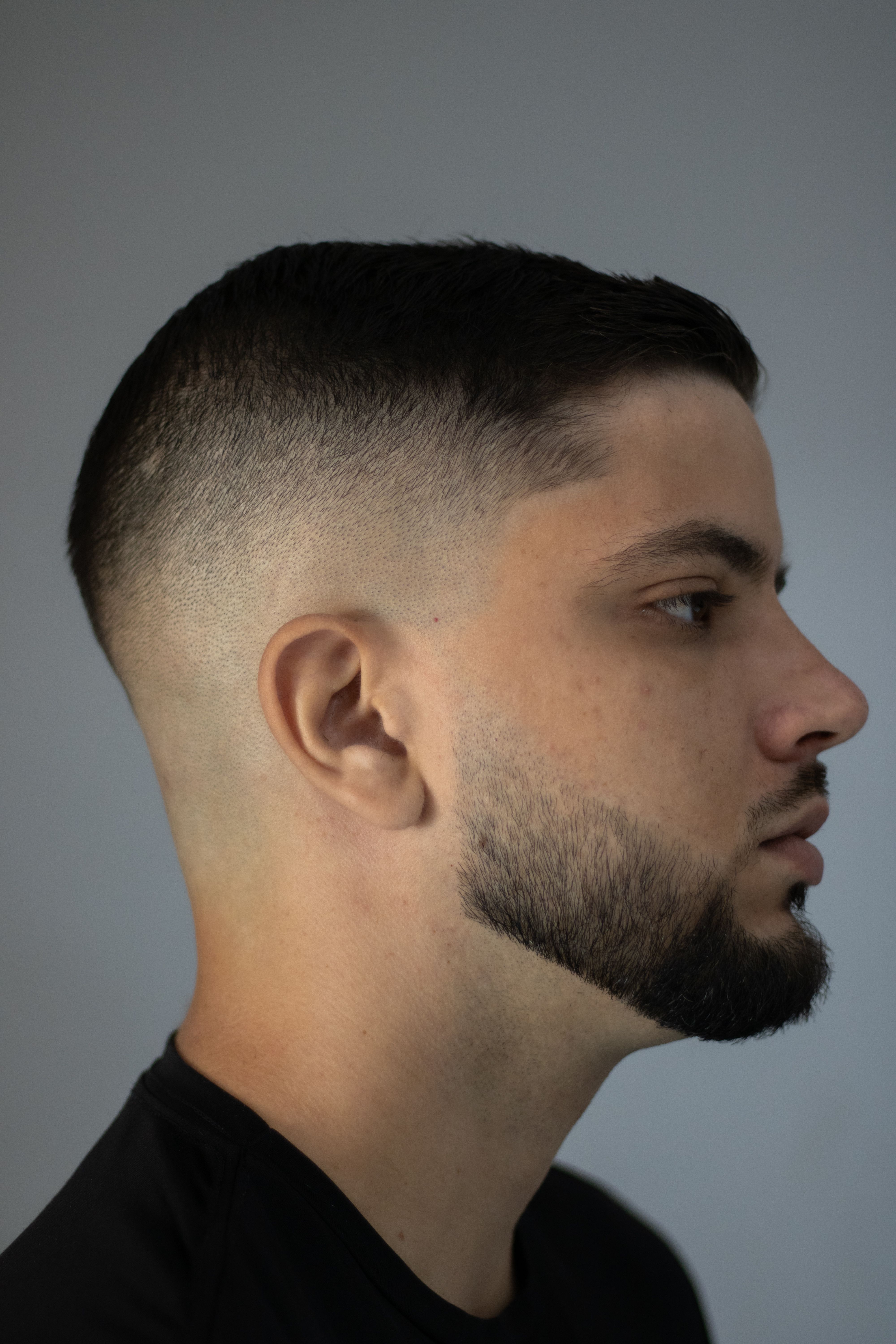 Profile view of a young man with a modern fade haircut and styled beard, showcasing sophisticated grooming.