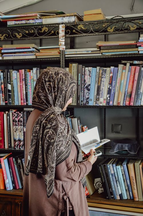 Free A woman in a hijab explores books on a vintage bookstore shelf. Stock Photo