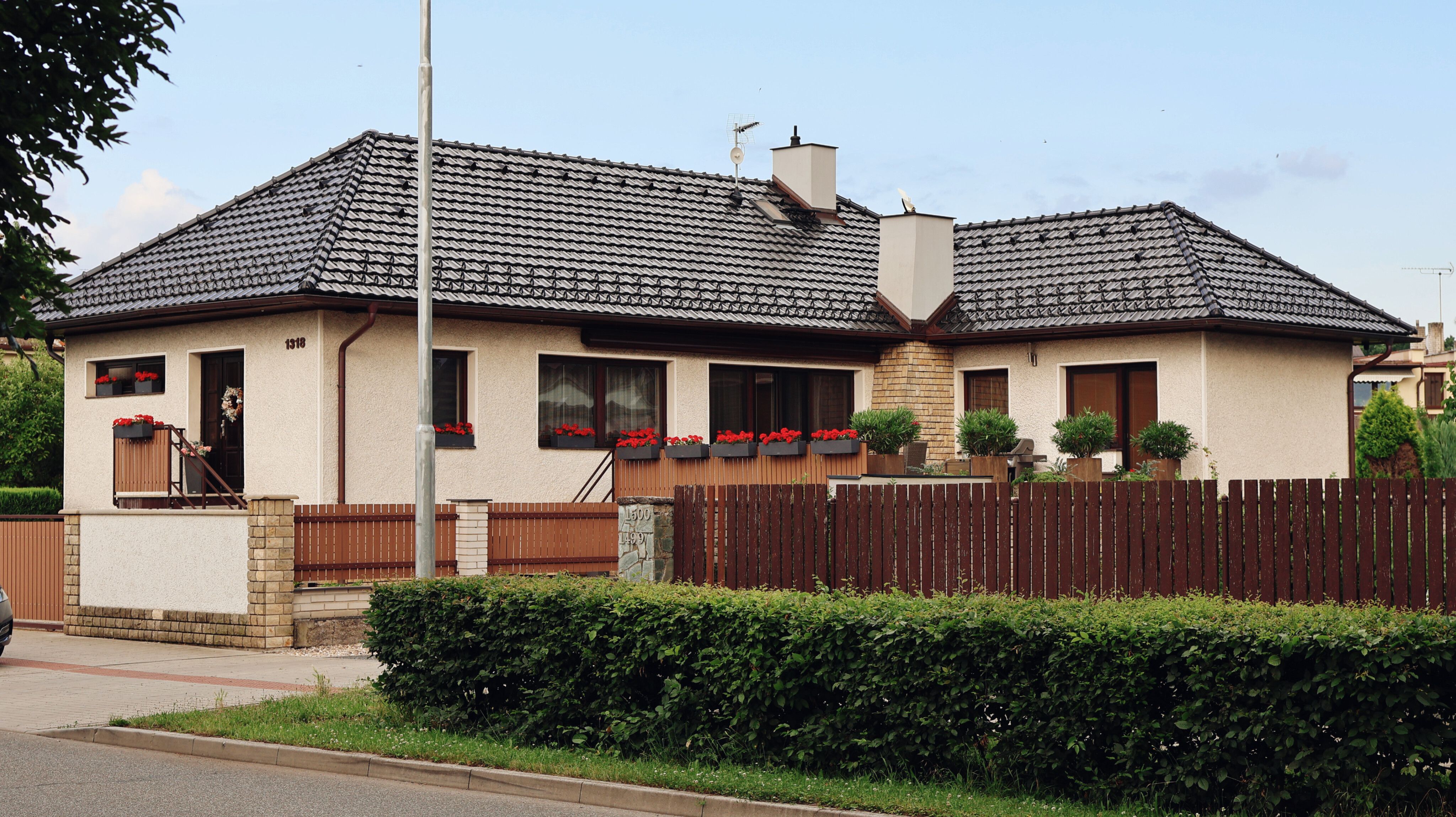 A cozy suburban house with a tiled roof, surrounded by a wooden fence and red flowers.
