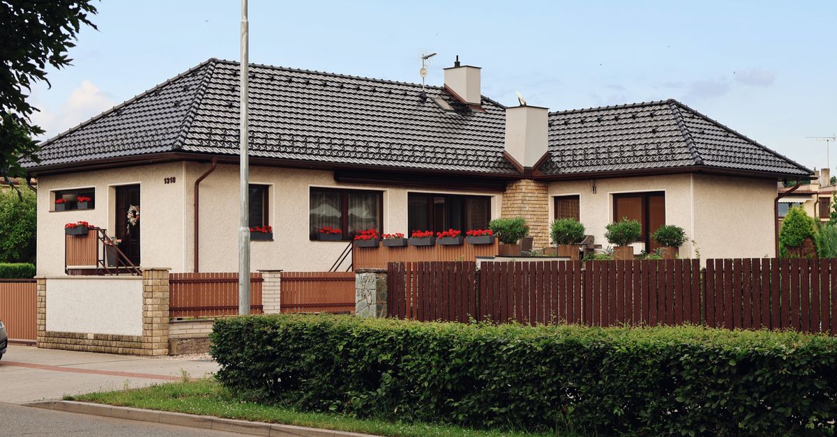 A cozy suburban house with a tiled roof, surrounded by a wooden fence and red flowers.