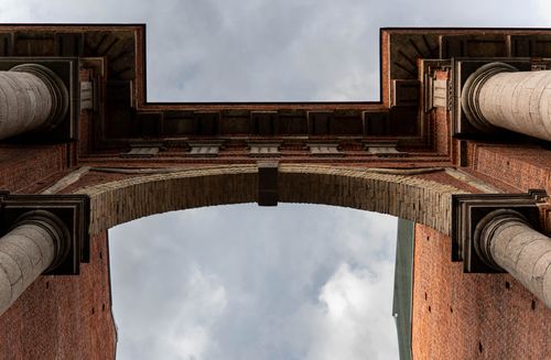 Free Upward perspective of a historic brick and column archway against a cloudy sky, showcasing architectural symmetry. Stock Photo