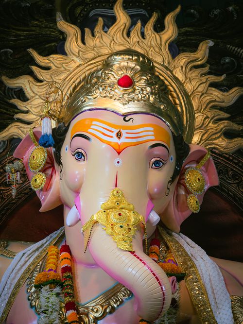 Free Vibrant Ganesh idol adorned with gold crown and floral garlands, showcasing intricate craftsmanship. Stock Photo