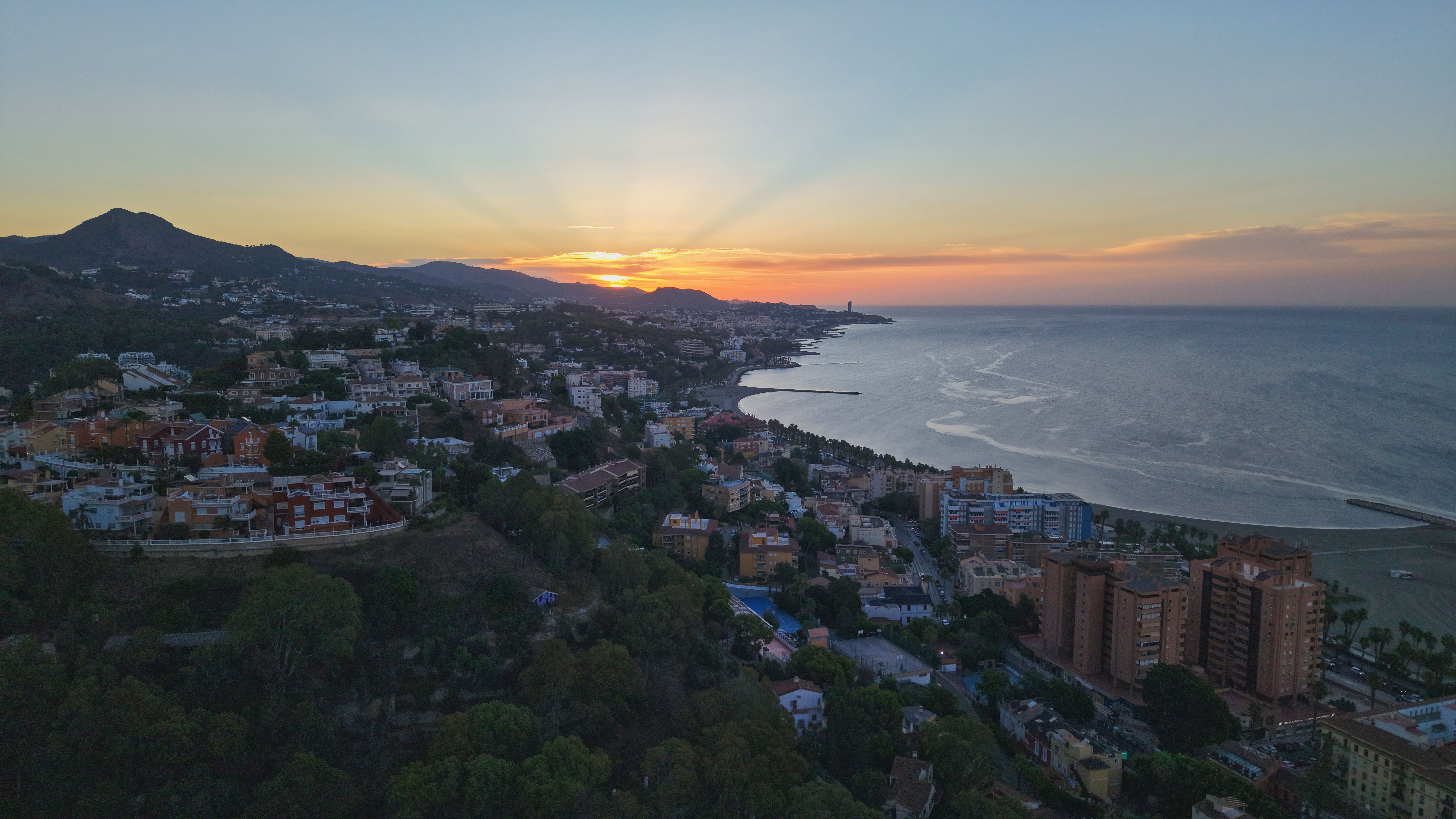 Captivating aerial view of Málaga cityscape at sunset with mountains and coastline.