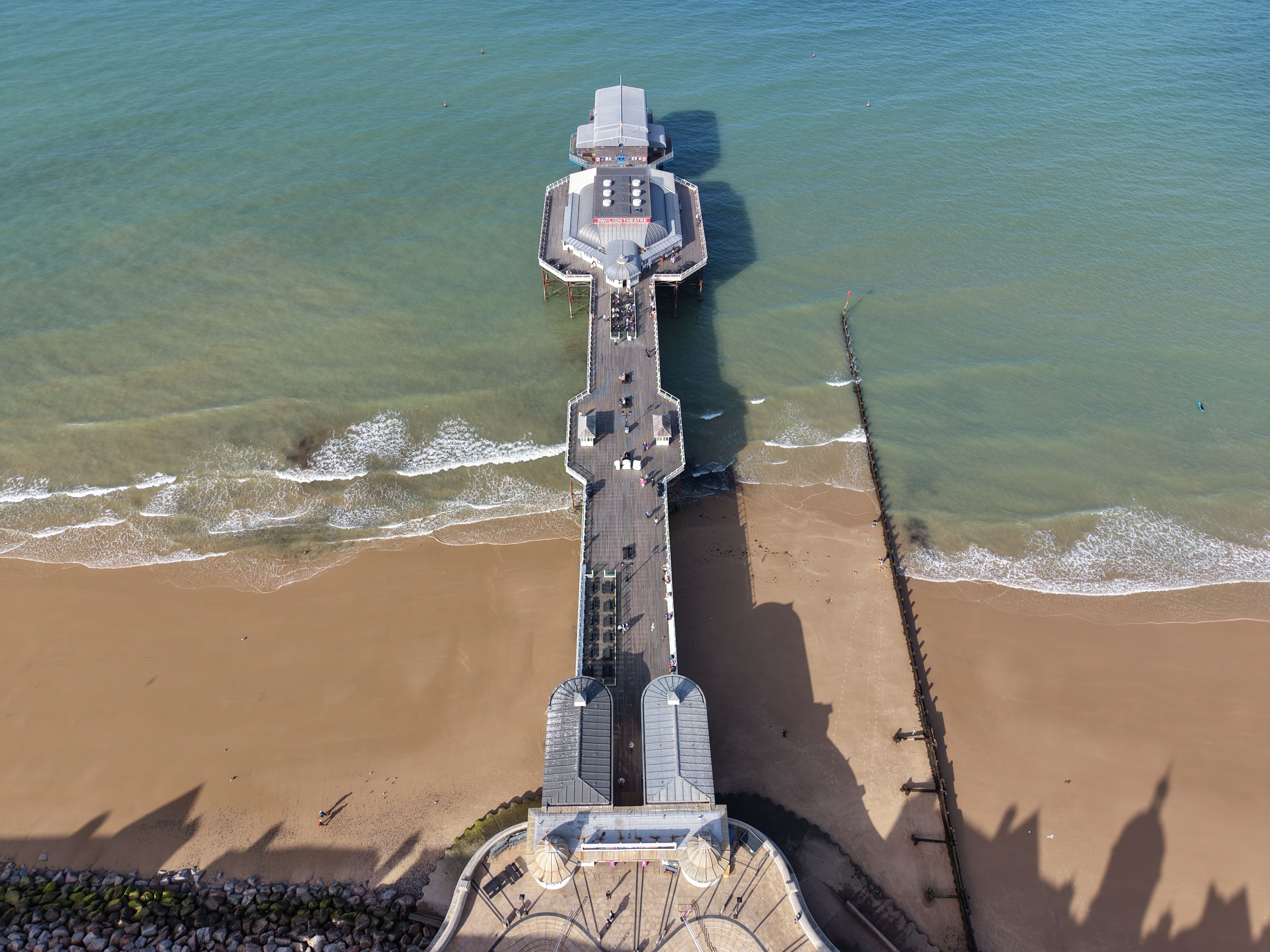 Drone shot capturing Cromer Pier and sandy beach on a sunny day, highlighting the beautiful coastline.