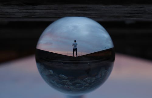 Круглый стеклянный шар, отражающий стоящего человека