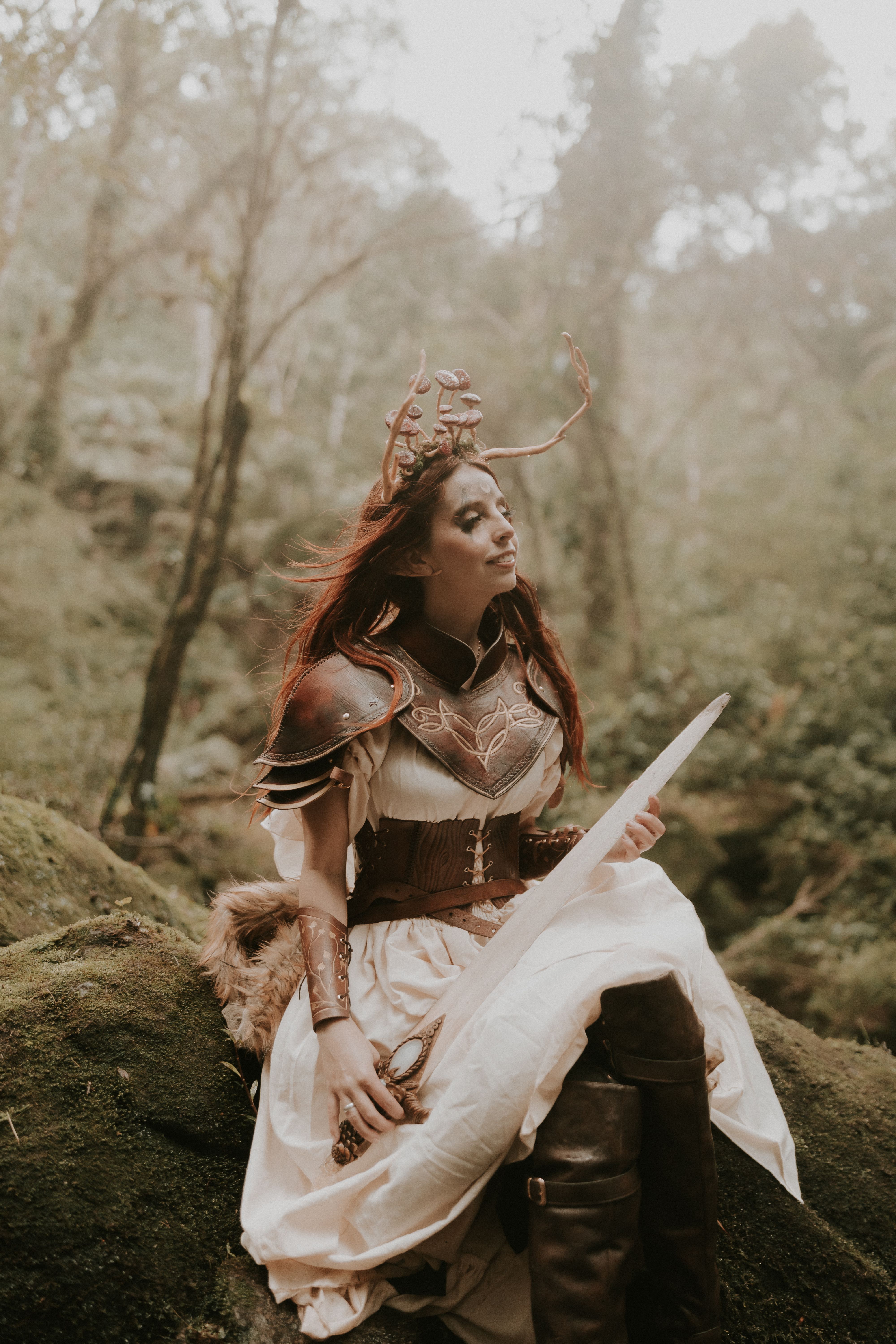 A fantasy warrior woman in leather armor sits on a rock in an enchanted forest setting.