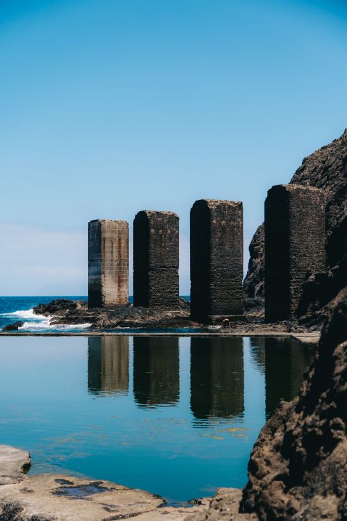 Free Image of stone pillars reflected in a natural pool in Hermigua, highlighting dramatic coastal landscape. Stock Photo