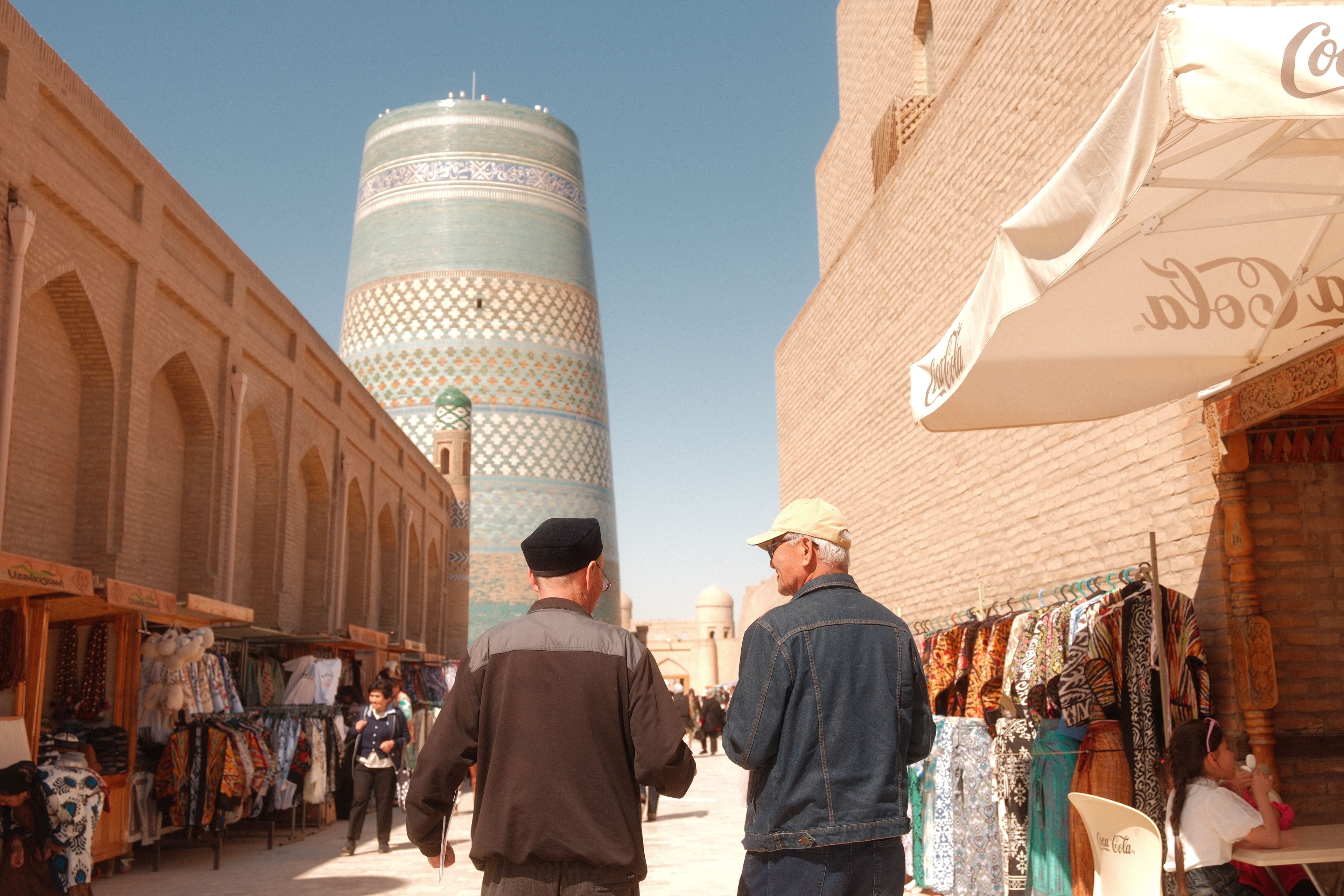 Vibrant street scene in Khiva, Uzbekistan, featuring local shoppers and the iconic unfinished minaret.