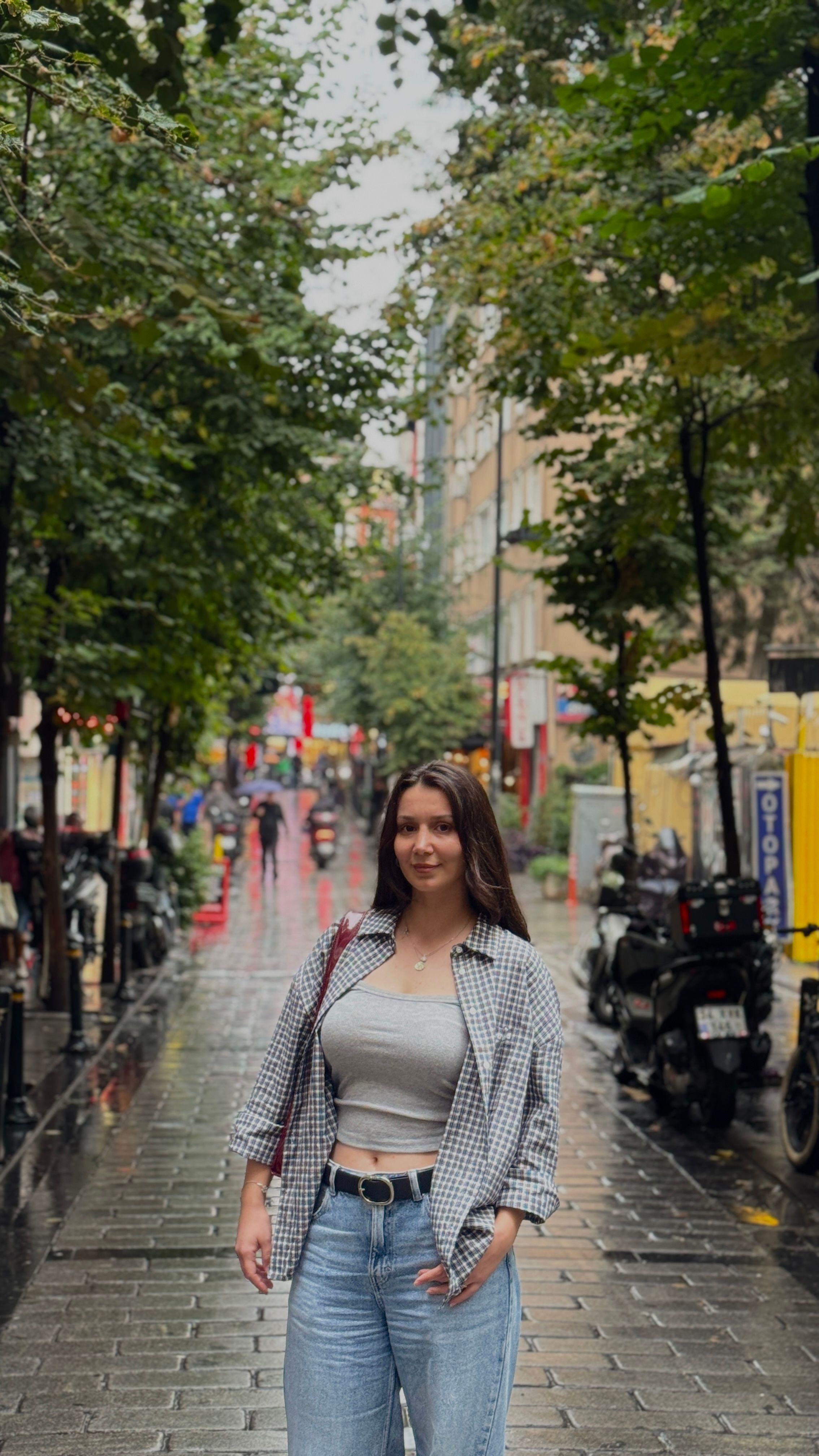 Woman strolling on a rain-soaked street lined with trees in Istanbul, capturing urban life.