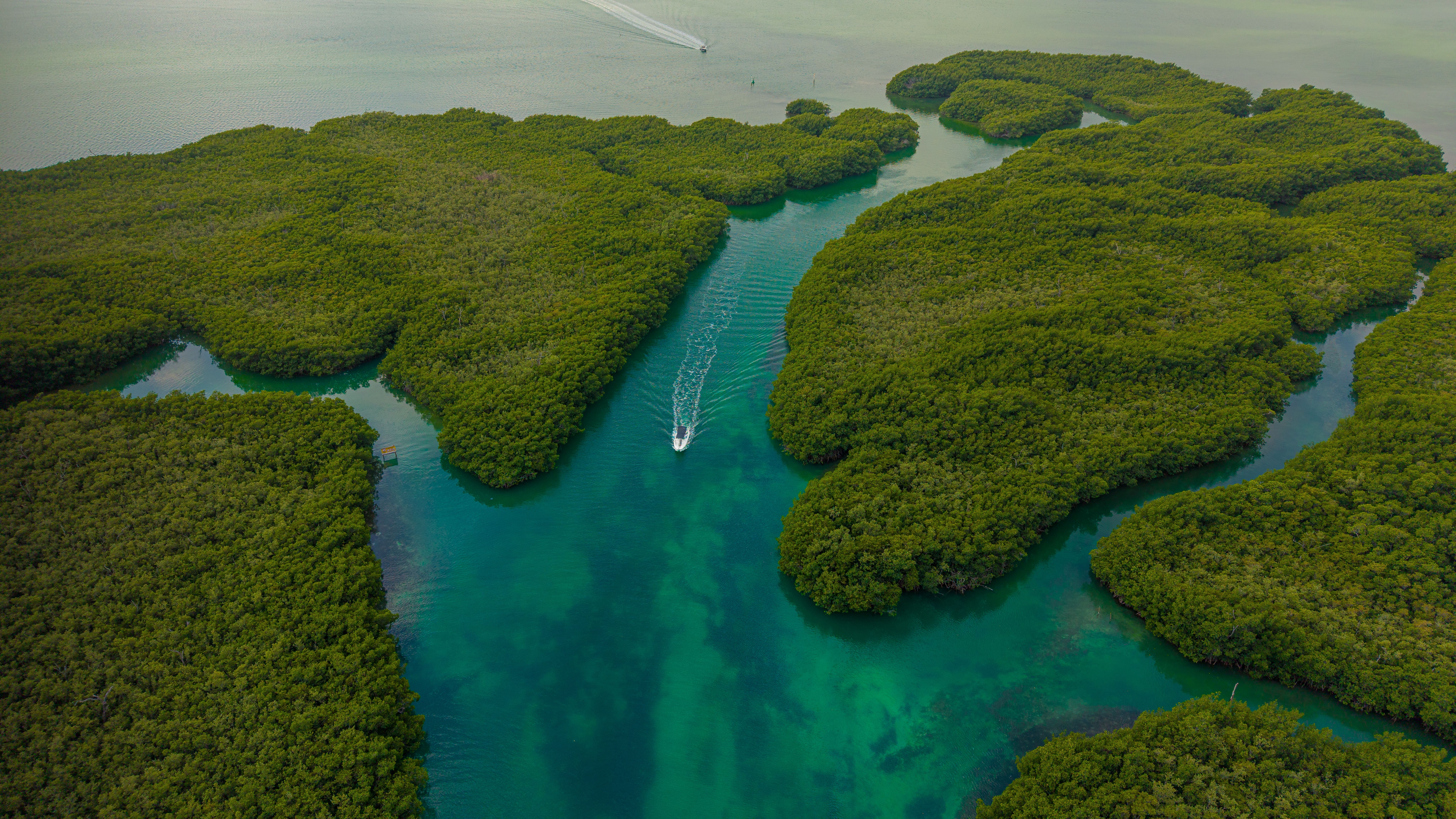 Aerial view of a small boat crossing a turquoise channel between mangrove islands, the kind of lagoon the Holbox three islands tour crosses