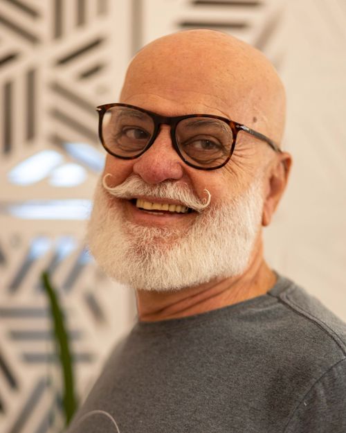 Free Portrait of a smiling elderly man with a white beard, glasses, and a patterned background. Stock Photo