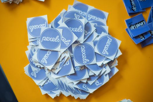 Pile of blue Pexels stickers on a vibrant yellow surface, top view.