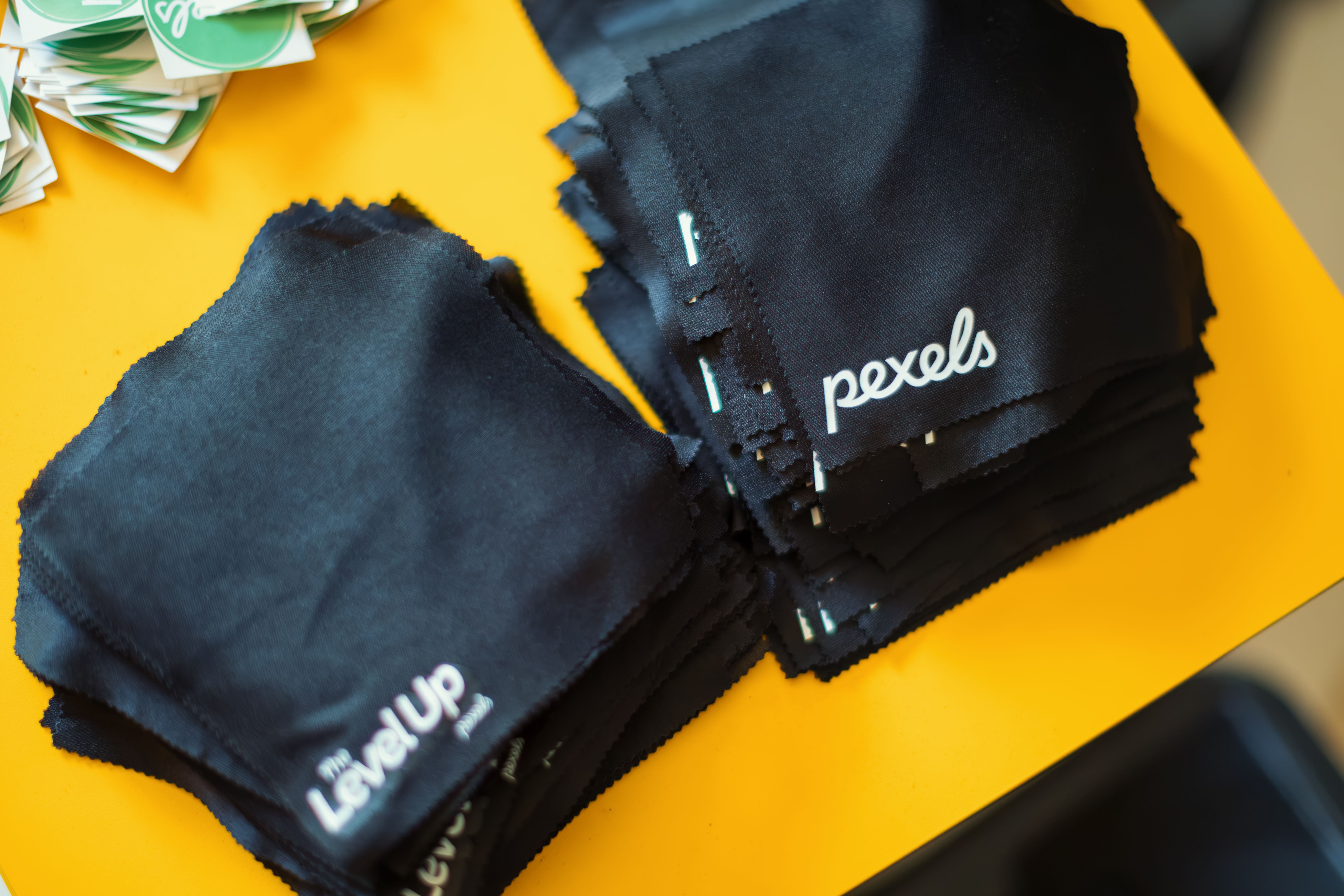 Stacked black microfiber cleaning cloths with branding on bright yellow background.
