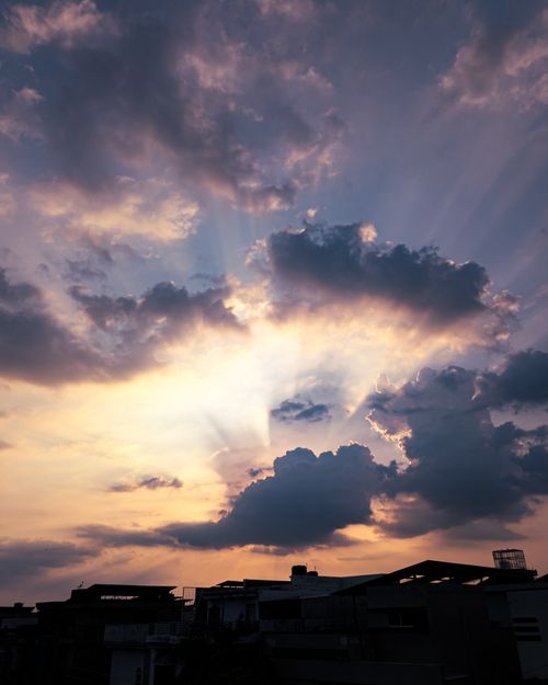 Free Dramatic sunset with sunbeams breaking through clouds over urban skyline. Stock Photo