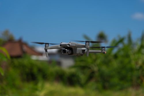 Free Quadcopter drone flying over a green field under a blue sky, capturing aerial views. Stock Photo