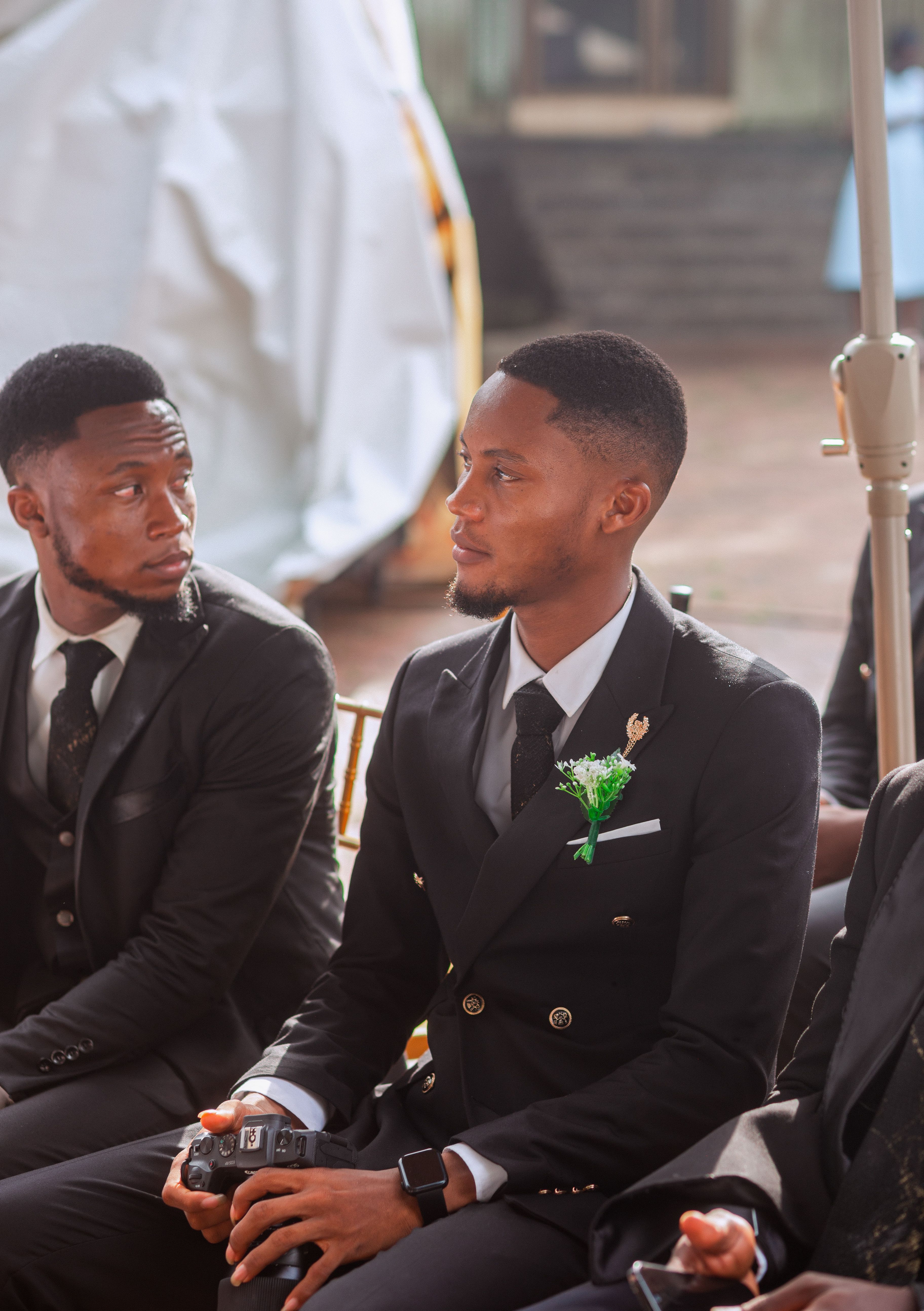 Two young men in suits attending a formal event, seated indoors.