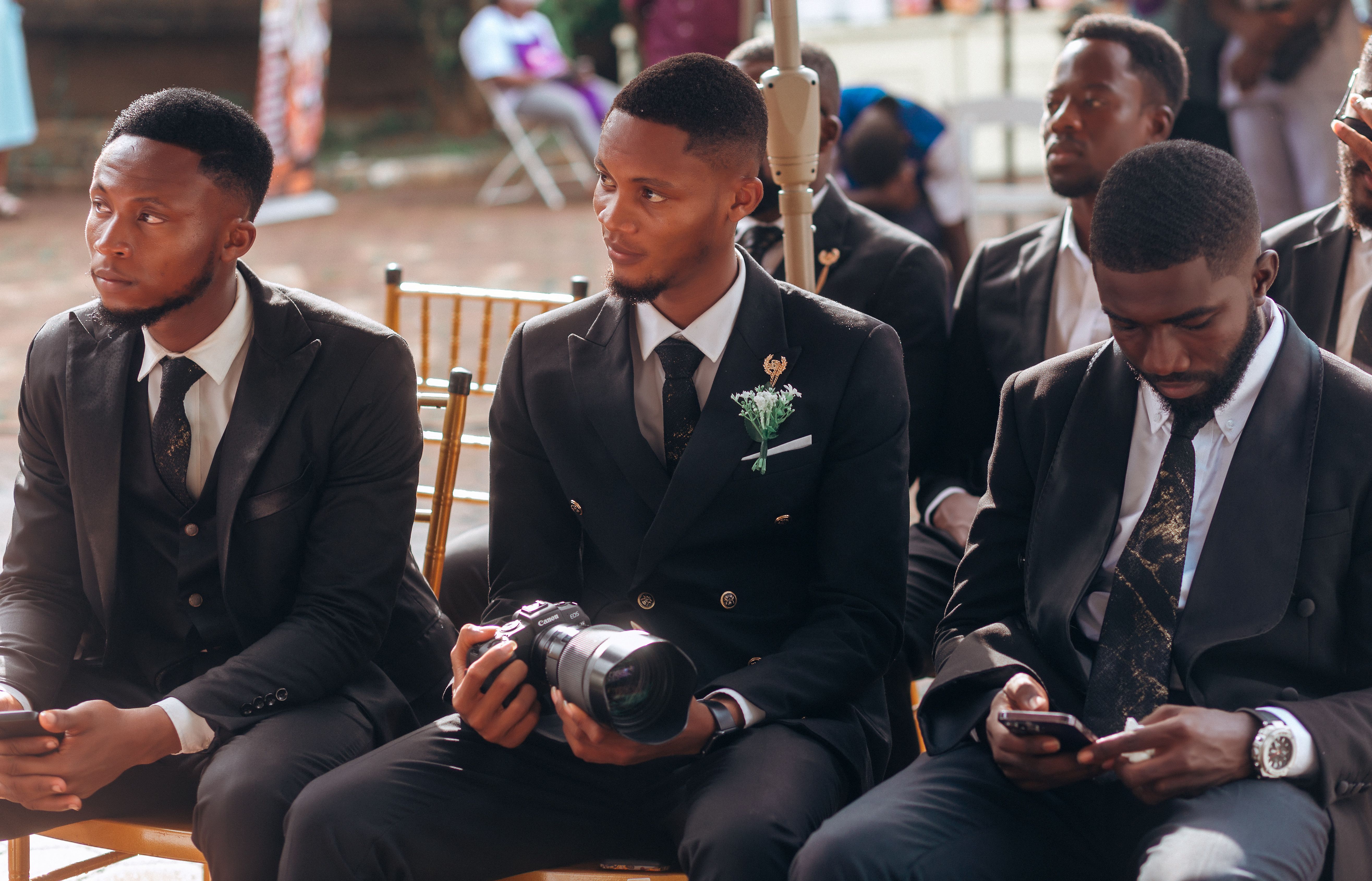 Group of men in formal suits attending an outdoor event, capturing moments.