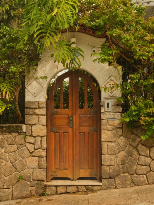 Free An inviting stone archway with a rustic wooden door surrounded by lush greenery. Stock Photo