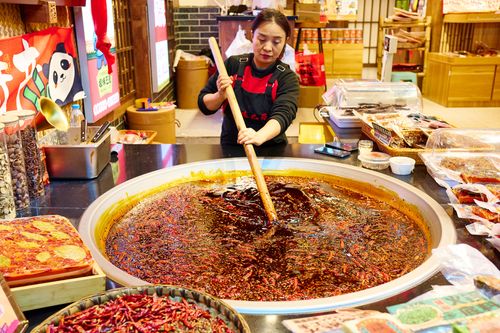 Free Woman stirring large pot of spicy hot pot in a bustling Asian market. Stock Photo