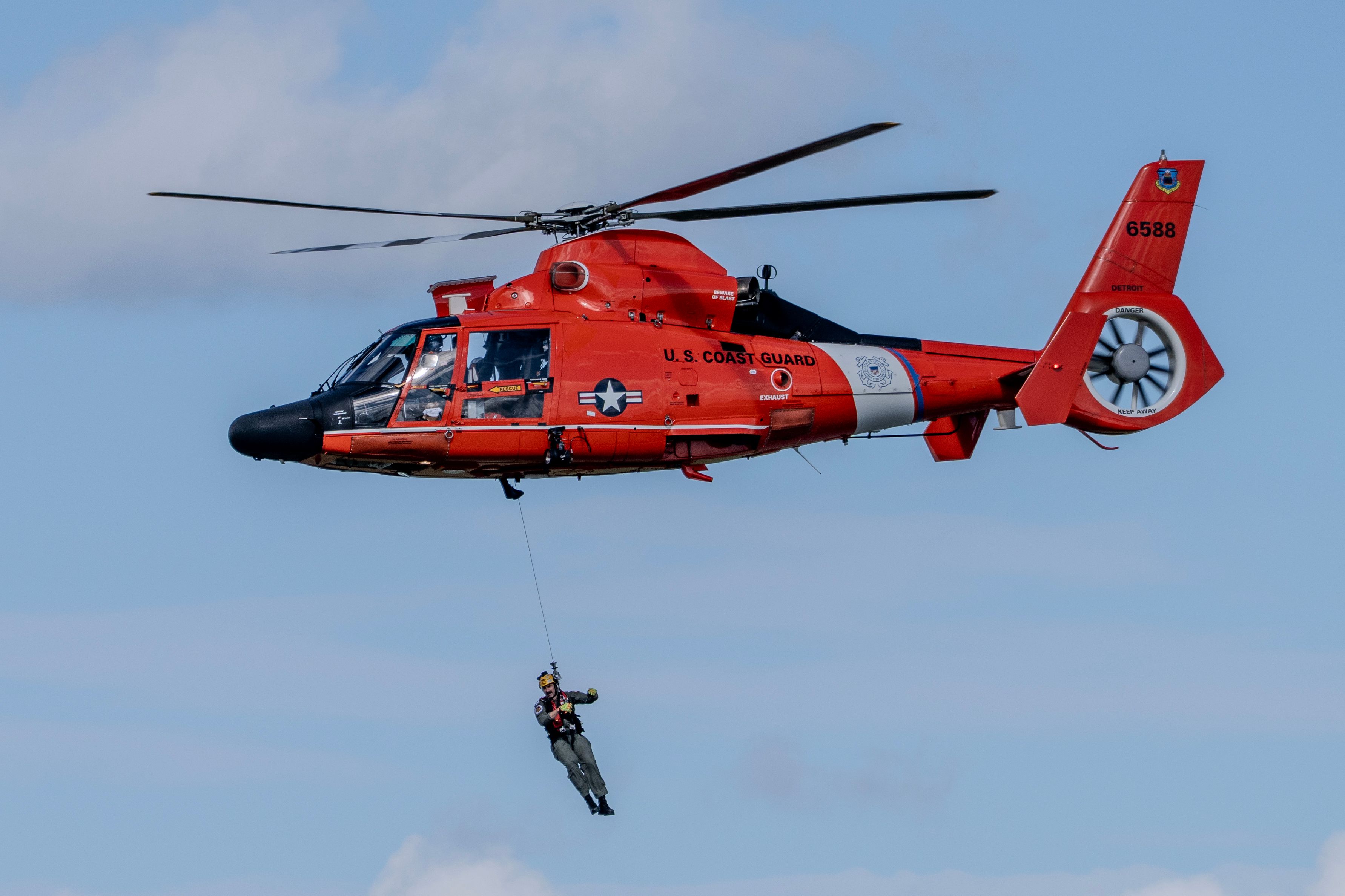 US Coast Guard helicopter conducting a mid-air rescue operation with a coast guard member on a rope.