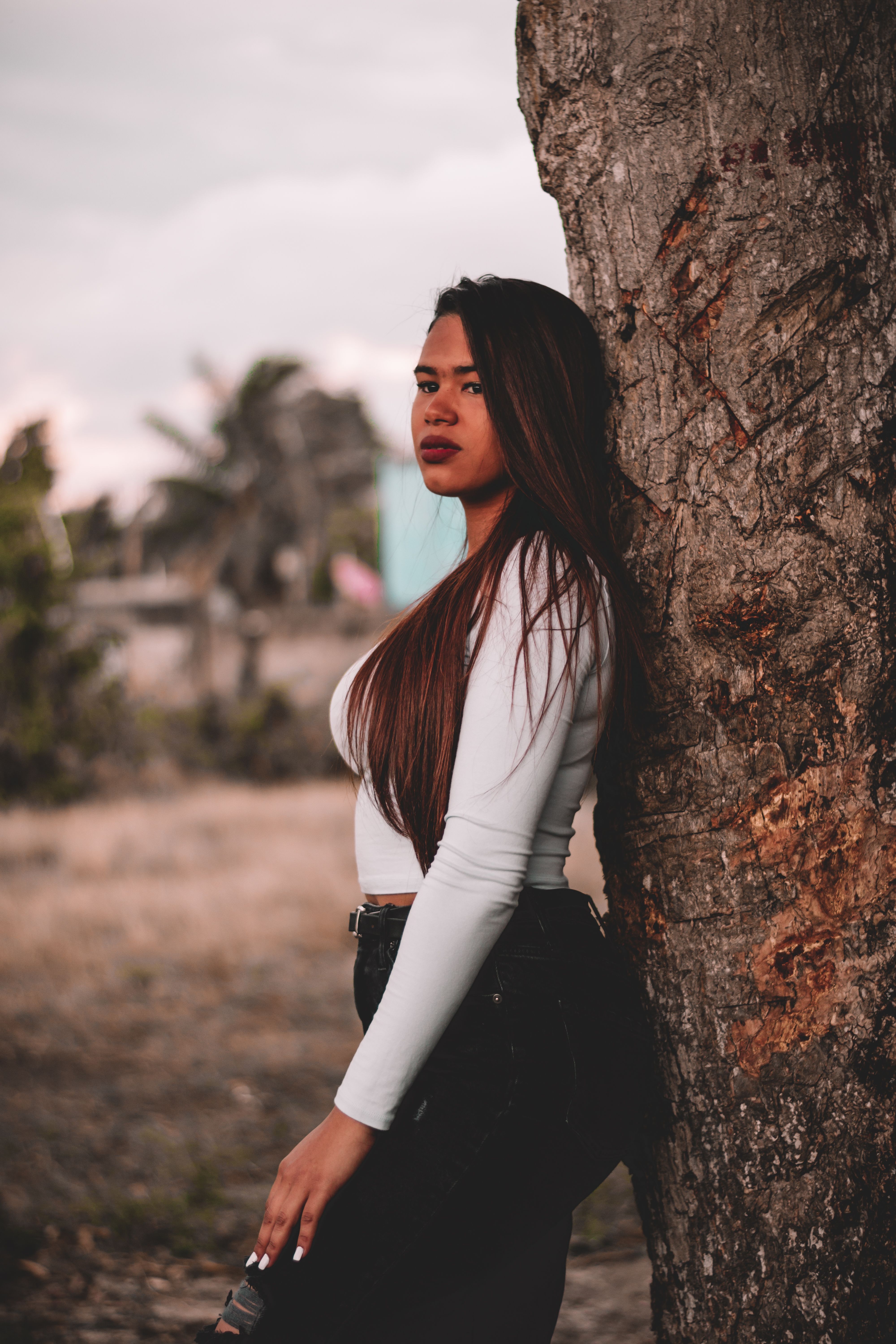 Woman in casual attire leaning against tree at twilight