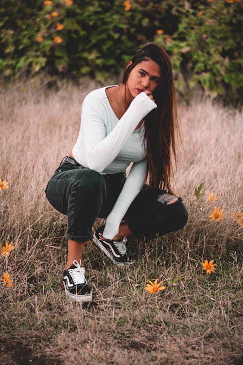 Woman in White Long Sleeve Shirt and Black Pants Sitting on Brown Grass Field