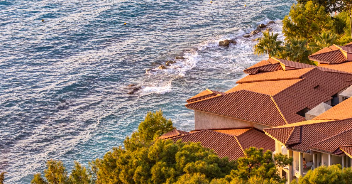 Mediterranean villas with orange roofs next to a clear sea coastline bathed in warm daylight.