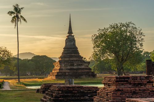 Free A stunning view of an ancient temple in Sukhothai Historical Park during sunrise, surrounded by lush greenery and ruins. Stock Photo