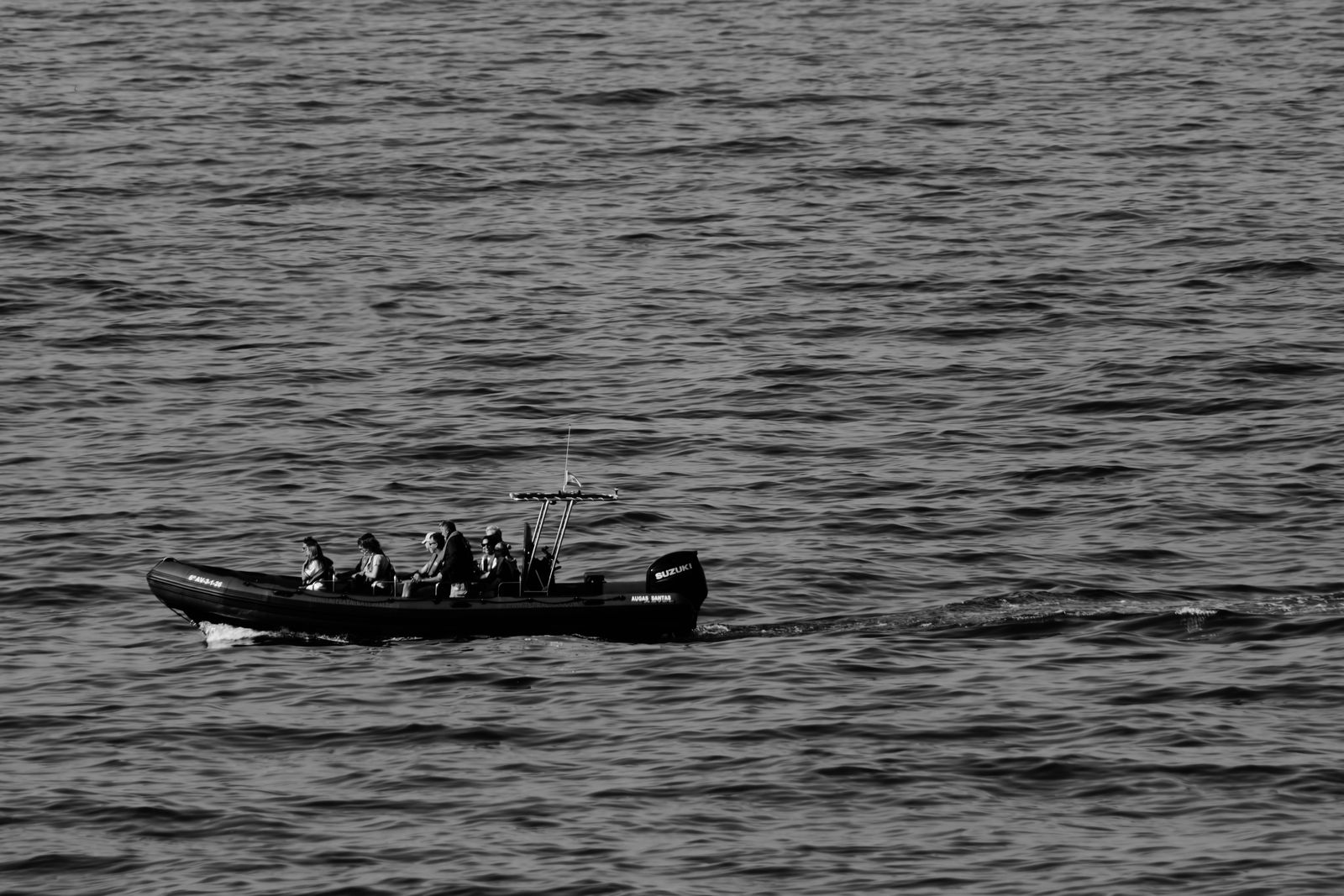 Petit bateau et passagers traversant une mer calme, près de Ribadeo, en noir et blanc