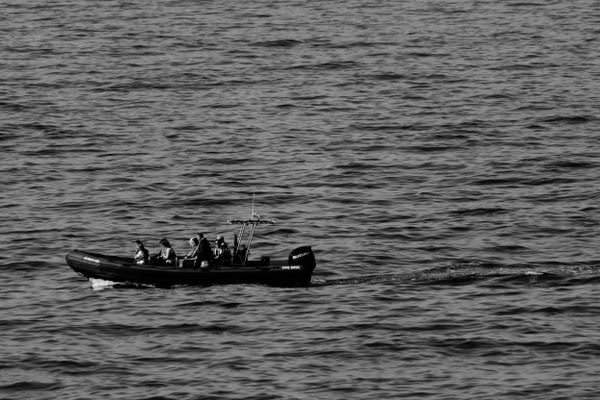 Petit bateau et passagers traversant une mer calme, près de Ribadeo, en noir et blanc