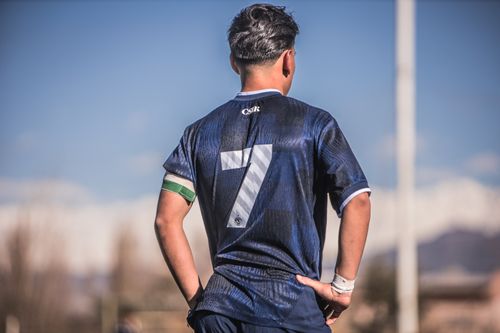 Free Young soccer player wearing a number 7 blue jersey stands on the field with a clear sky background. Stock Photo