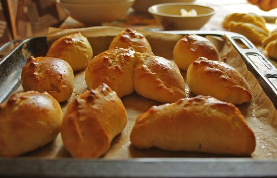 Golden brown homemade bread rolls fresh from the oven on a baking tray, showcasing home baking.