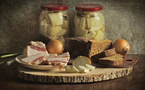 Free Traditional rustic scene featuring sliced bread, onions, bacon, and pickle jars on a wooden board. Stock Photo