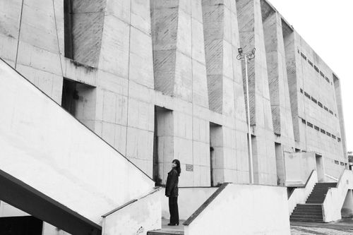Free A woman stands outside a brutalist concrete building, looking upward. Stock Photo