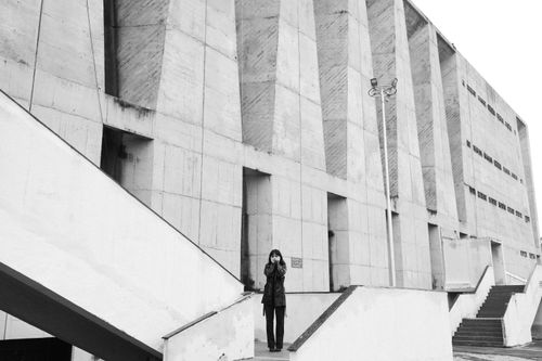 Free Black and white photo of a person posing near a brutalist concrete building. Stock Photo