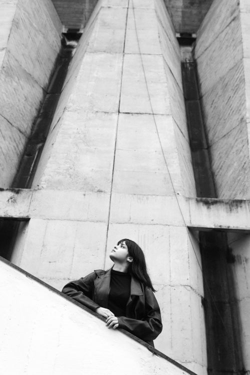 Free Black and white photo of a woman standing against a dramatic architectural structure. Stock Photo