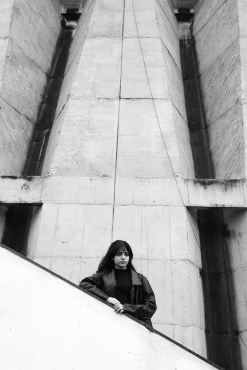 Free A woman leans against a concrete building in a moody black and white portrait. Stock Photo