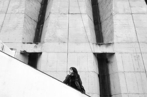 Free A young woman stands pensively by a large concrete structure, showcasing urban modernity. Stock Photo