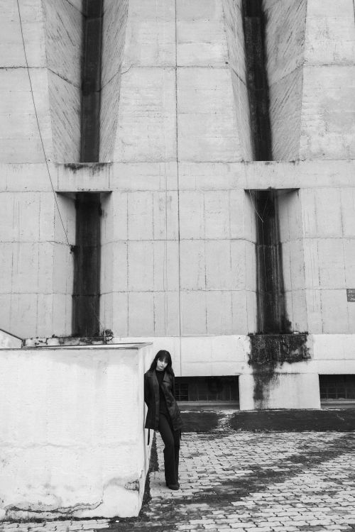 Free A moody black and white portrait of a person standing near a large concrete structure. Stock Photo