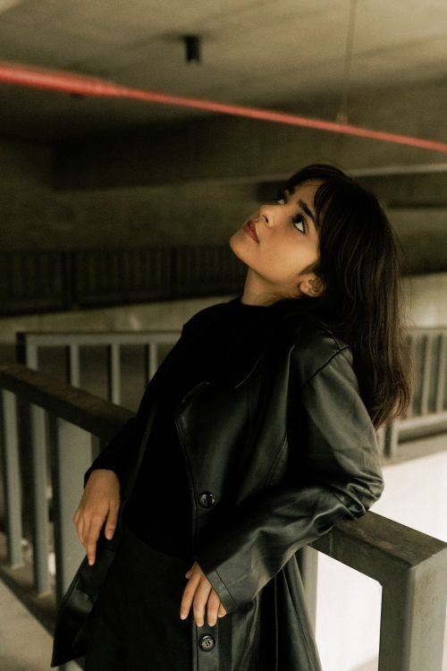 Free Young woman in leather jacket gazing upwards, urban environment. Stock Photo