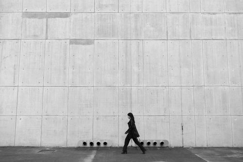 Free Black and white photo of an individual walking alongside a minimalist concrete wall. Stock Photo