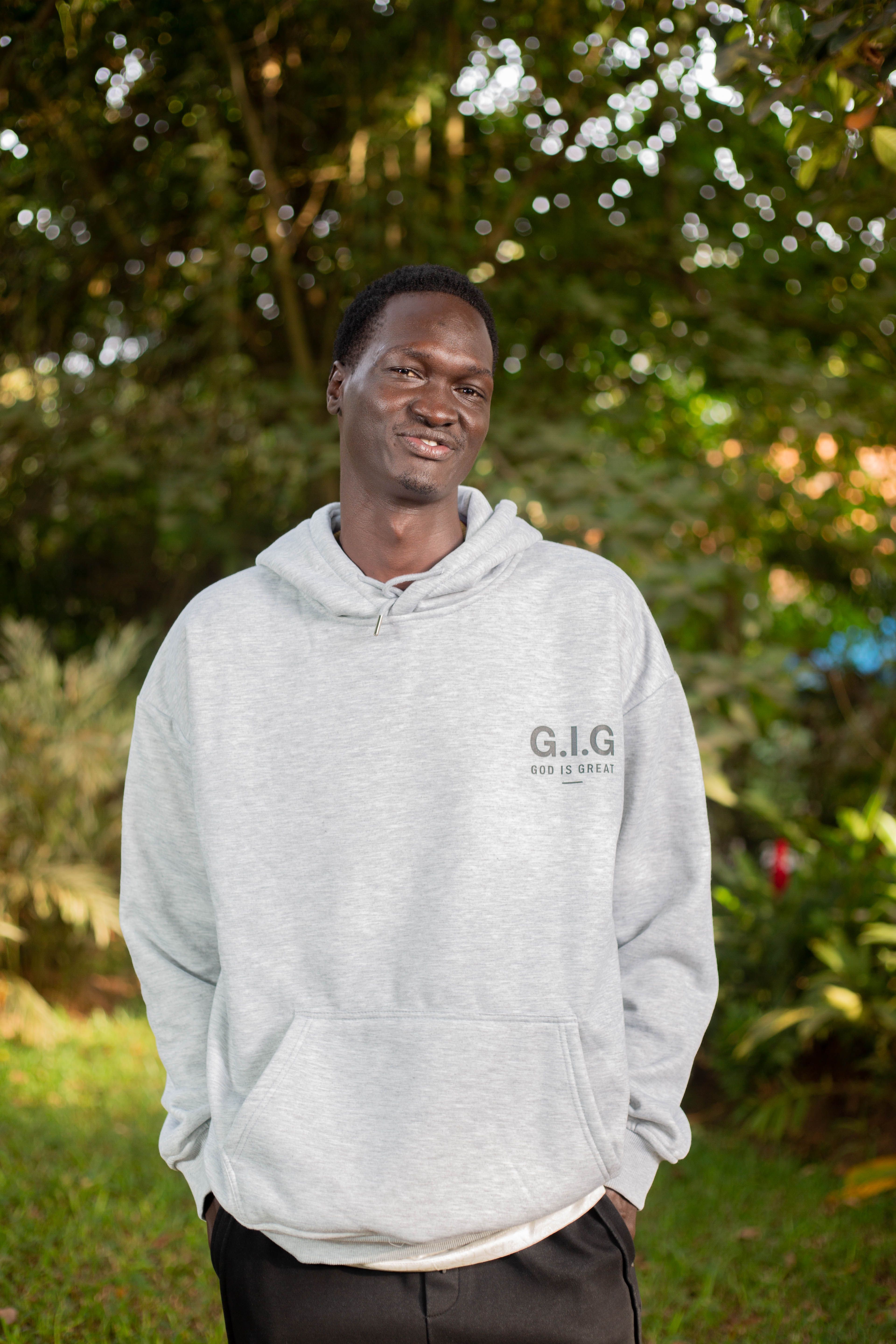 Casual outdoor portrait of a smiling man in a hoodie, surrounded by greenery.