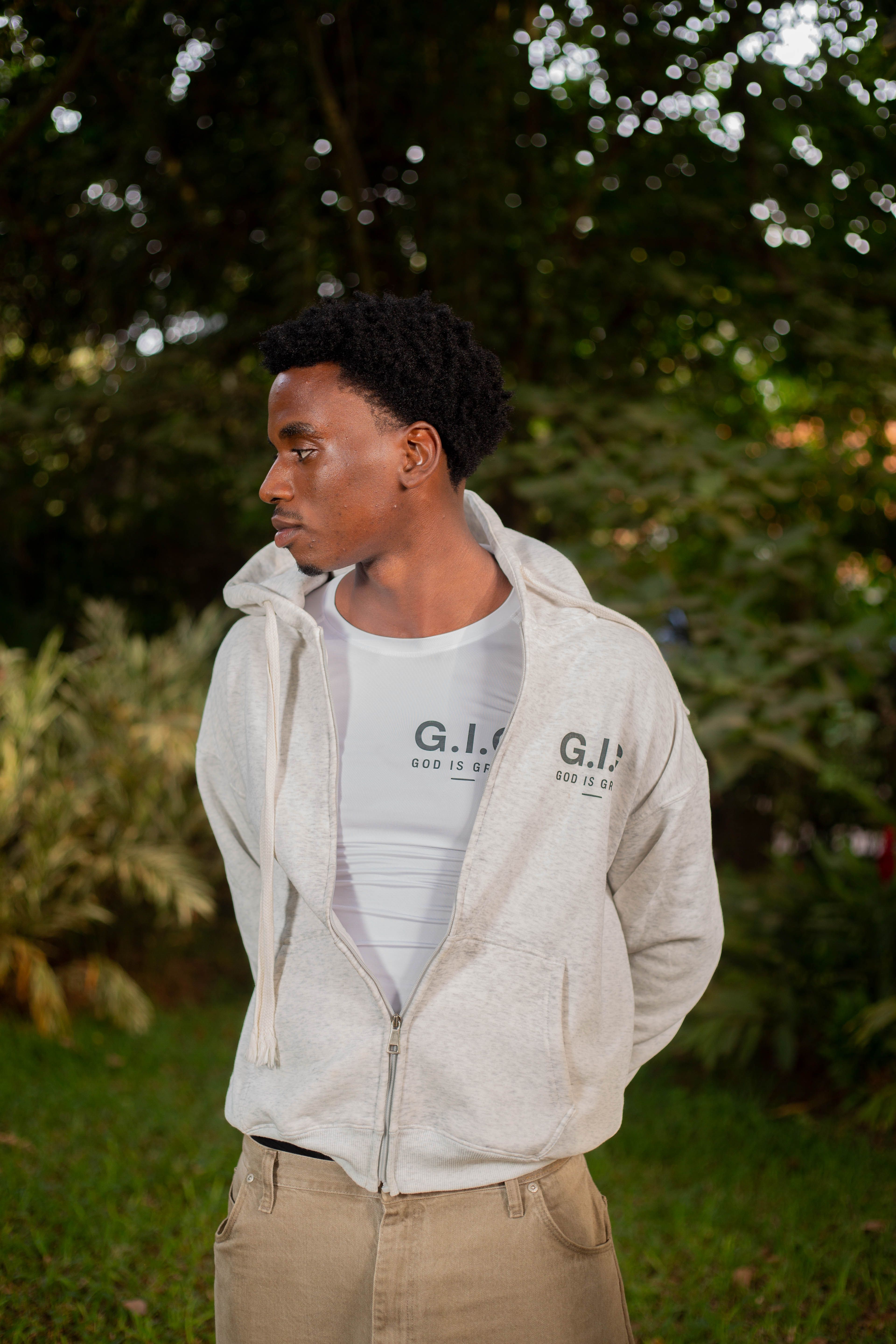 Man wearing a hoodie standing outdoors, surrounded by greenery. Casual and relaxed vibe.