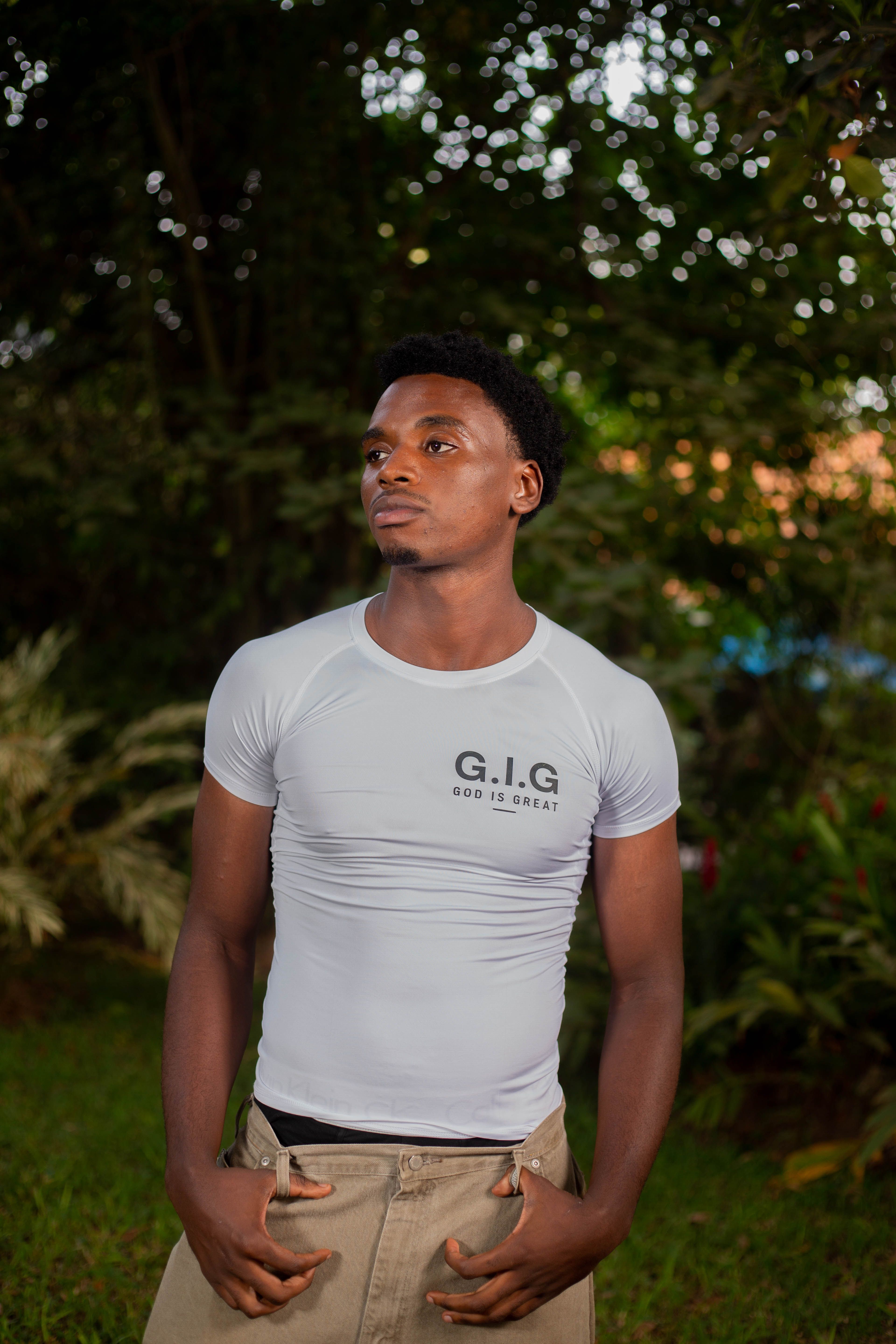 Young man standing confidently outdoors in a G.I.G. t-shirt, surrounded by greenery.