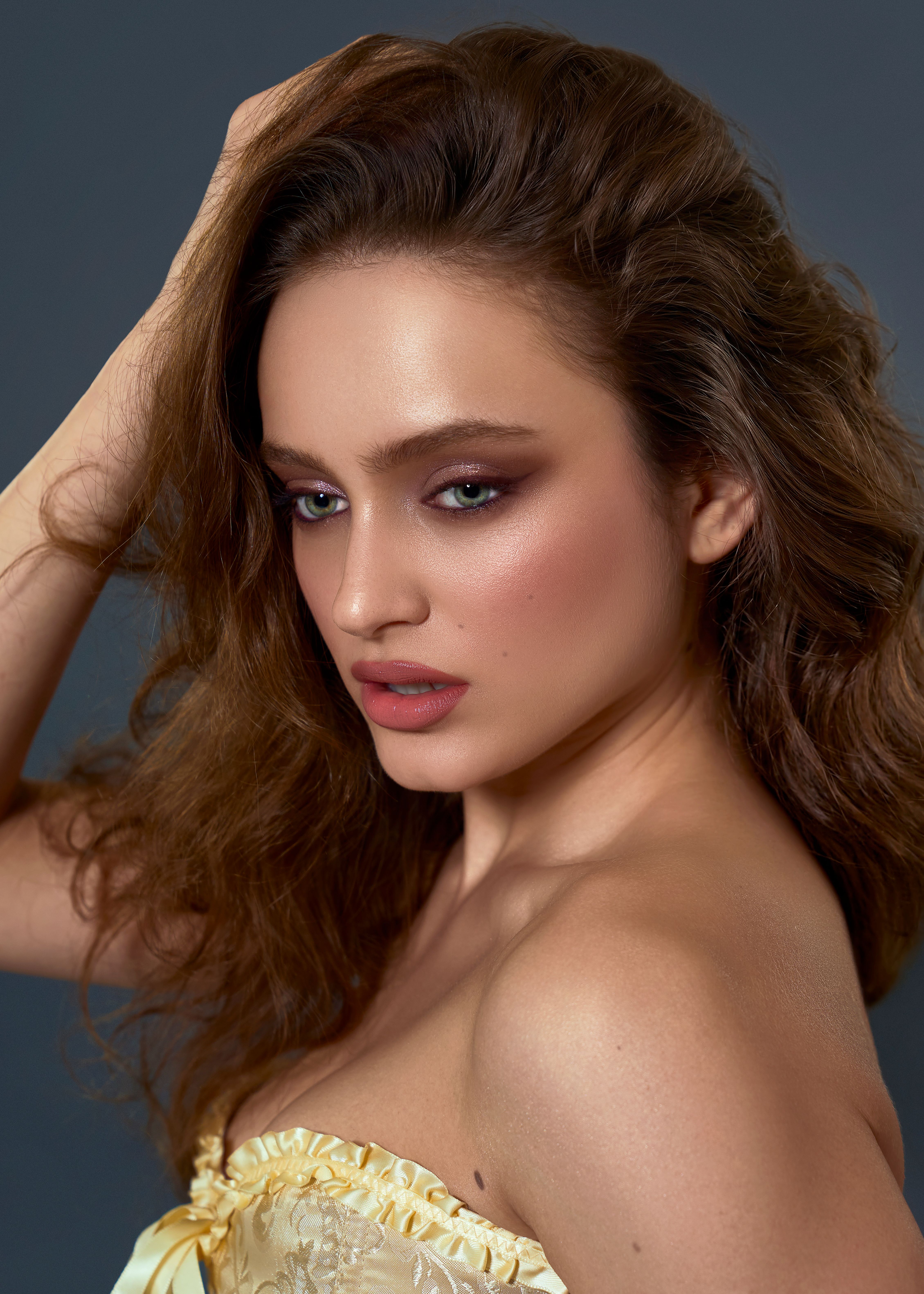 Close-up portrait of a woman with glamorous makeup and wavy hair against a dark background.
