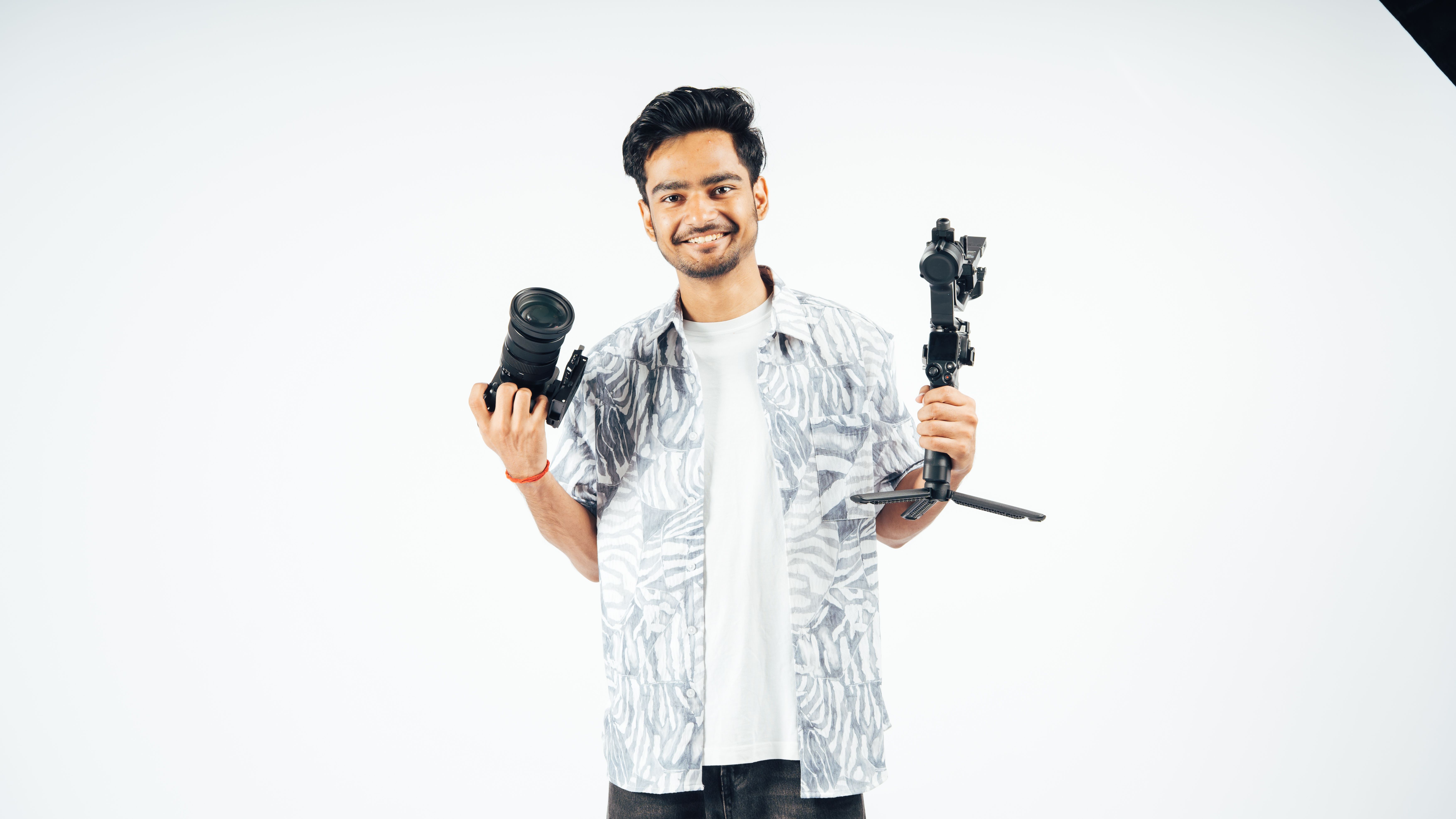 A cheerful photographer poses with a camera and gimbal against a plain backdrop.