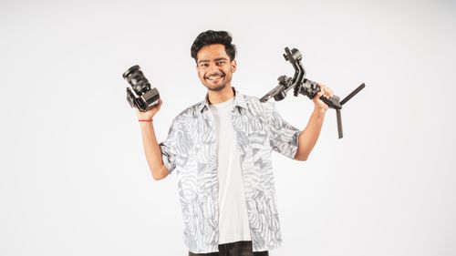 Free Portrait of a smiling filmmaker holding a camera and gimbal, showcasing filmmaking equipment. Stock Photo