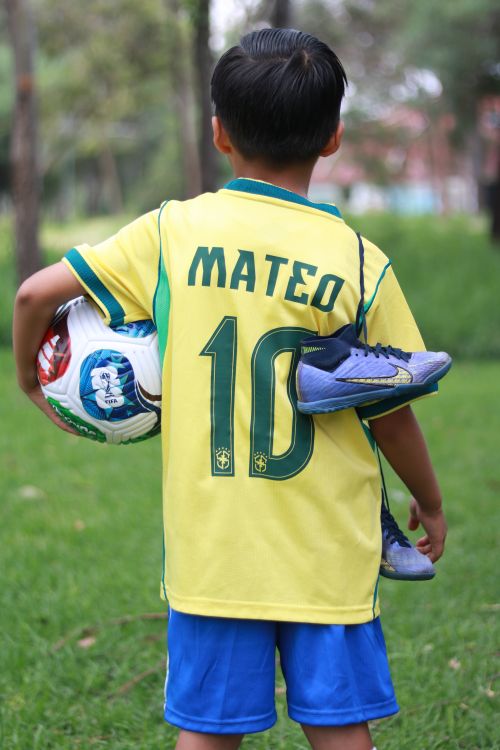 Free Back view of a child soccer player holding a ball outdoors. Stock Photo